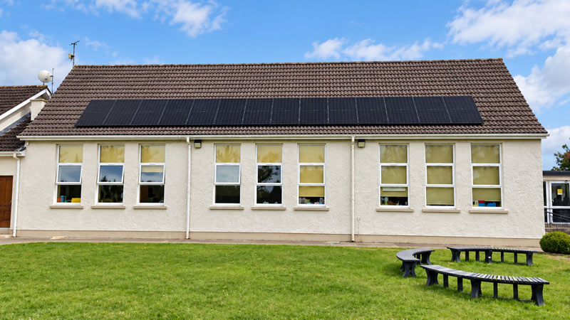 Solar Panels on Irish School Building Solar panels installed across the roof of an Irish school building with classroom windows and a green lawn.